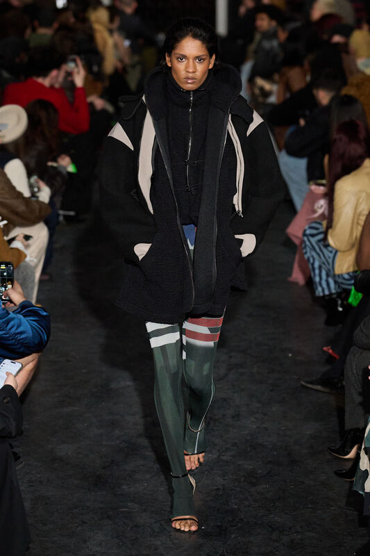 Модель в объемном черном пальто и леггинсах с яркими вставками, создающих динамичный и современный образ