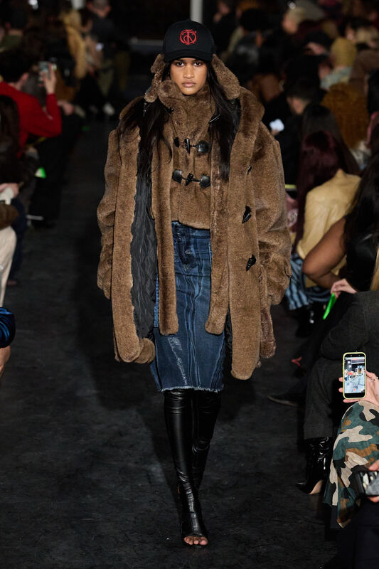 Объемный коричневый меховой пальто с капюшоном и джинсовая юбка, дополненные черной бейсболкой, создают уютный образ