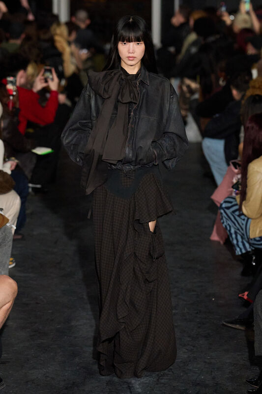 Кожаная блуза с объемным бантом и многослойная юбка в клетку, создают романтичный и загадочный стиль