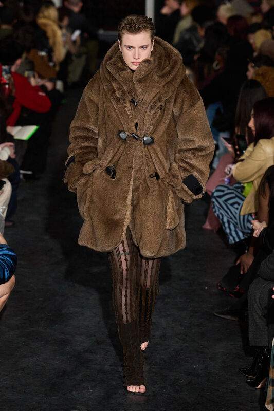 Уютный коричневый меховой плащ с крупным воротником, гармонирующий с облегающими прозрачными брюками