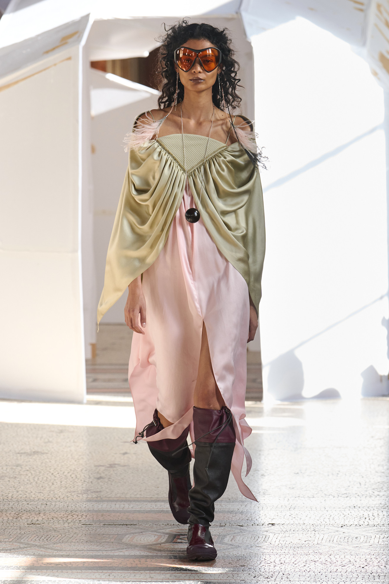 Модель в платье с зеленым верхом и розовой юбкой, украшенным перьями, завершает образ стильными очками