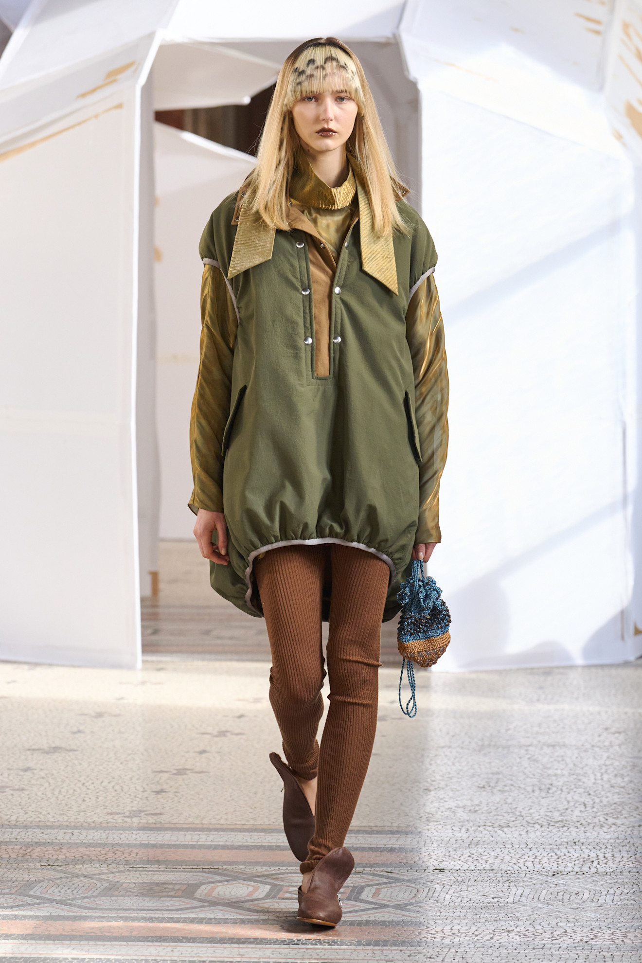 Объемная куртка оливкового цвета в сочетании с коричневыми леггинсами и текстурированной сумкой.