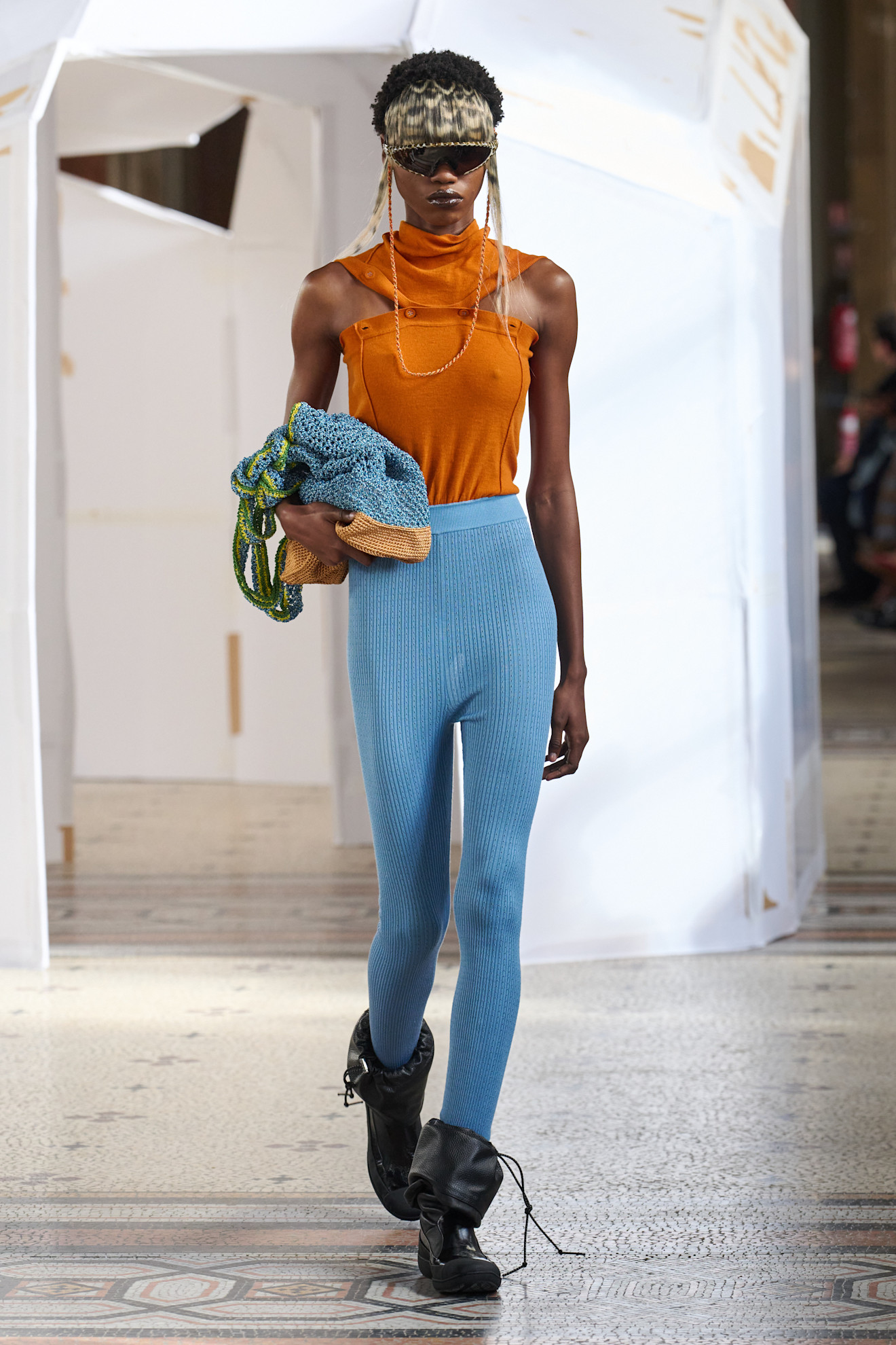 Оранжевая блуза с высоким воротником и голубые брюки в рубчик подчеркивают утонченность и современность.