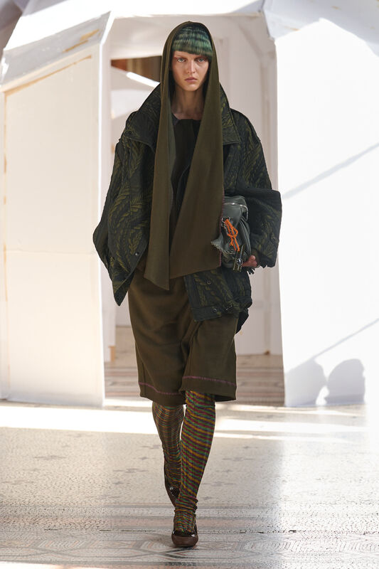 Модель в многослойном образе с капюшоном и яркими колготками, сочетает уют и современный стиль с акцентом на детали