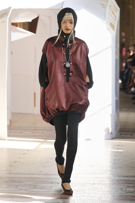 Объемный бордовый наряд с блестящей текстурой, дополненный черными леггинсами и стильным головным убором