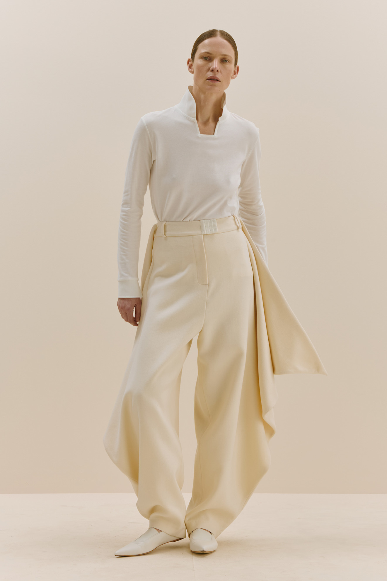 Минималистичный образ с белой водолазкой и широкими светлыми брюками, акцент на строгие линии и текстуру ткани.