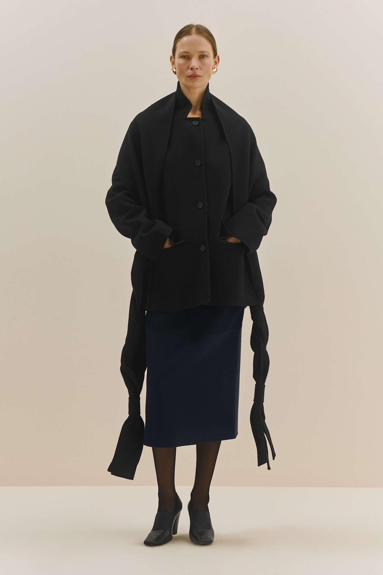 Объемный черный жакет с длинными рукавами и карманами, дополненный строгой юбкой и элегантными туфлями