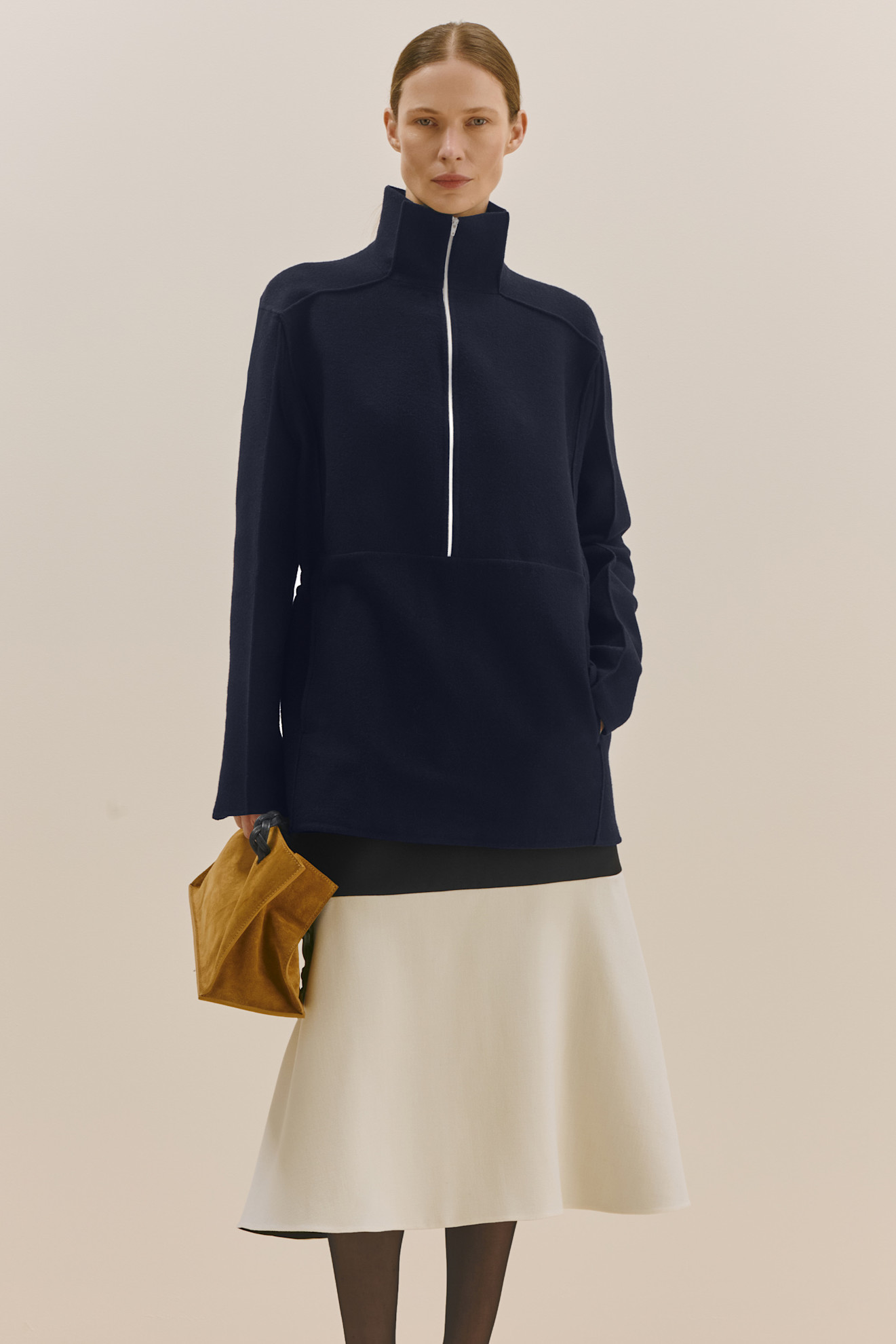 Темно-синий свитер с высоким воротником и молнией, в сочетании с юбкой и замшевой сумкой в руках