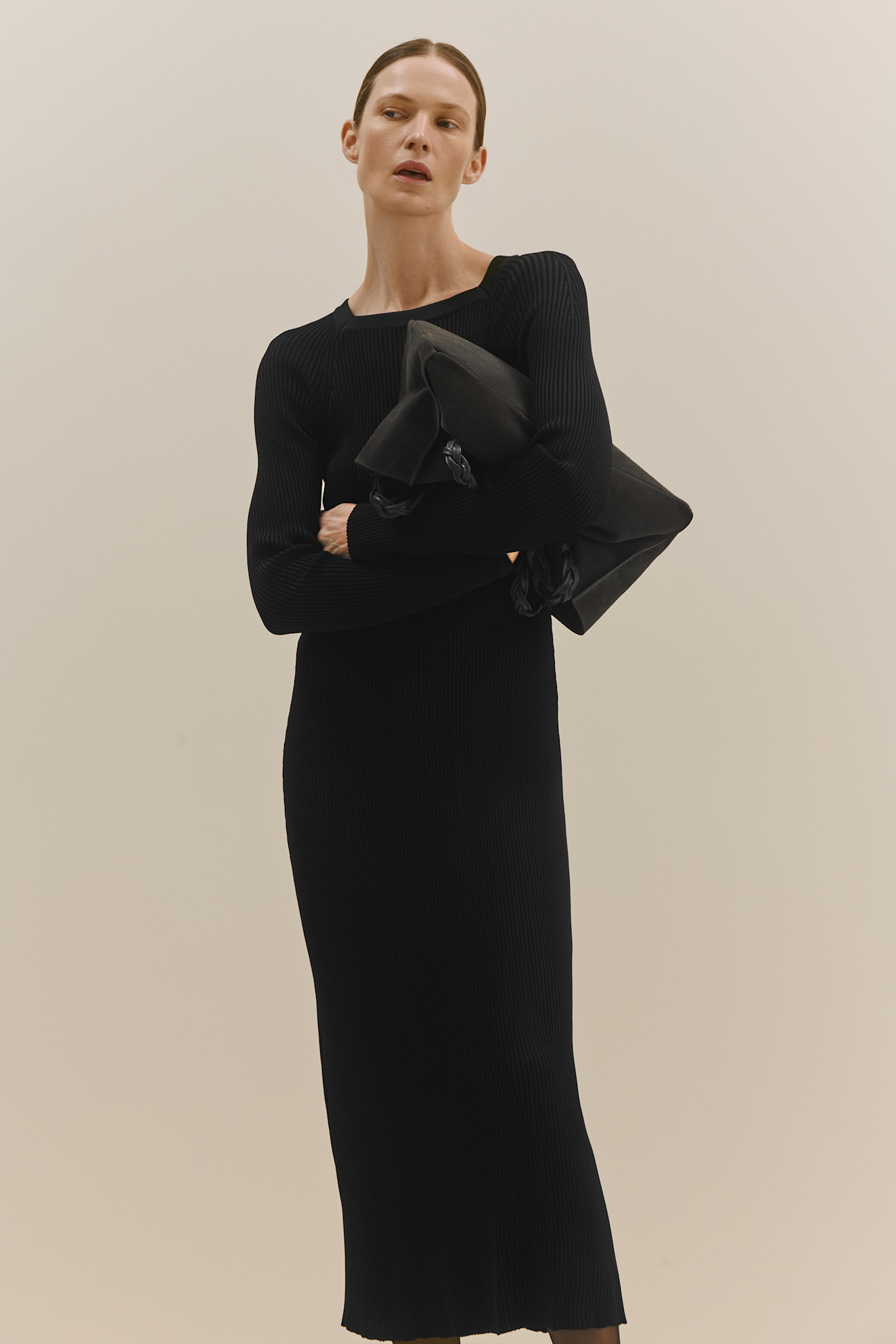 Черное вязаное платье с длинными рукавами и рифленой текстурой, в руках — стильная сумка в тон наряду