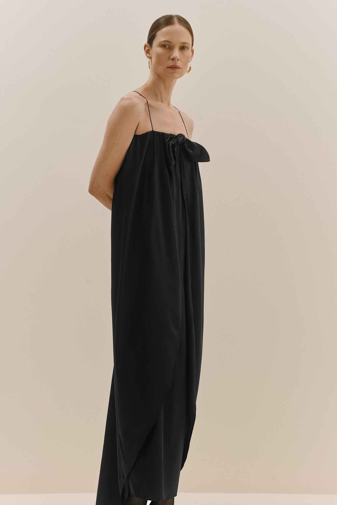 Элегантное черное платье с тонкими бретелями и бантом, подчеркивающее силуэт и создающее атмосферу утонченности