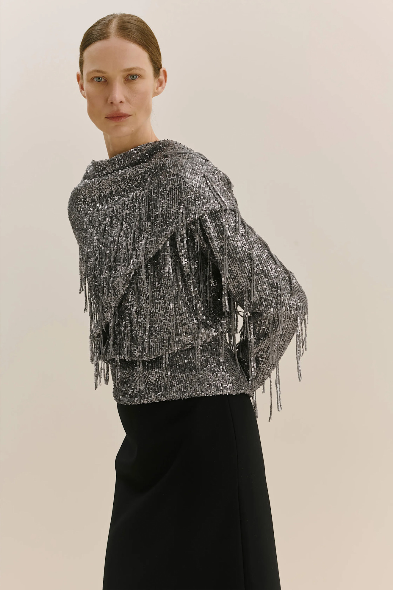 Серебристый топ с бахромой и блестками, гармонично сочетающийся с черной юбкой, создает стильный и вечерний образ