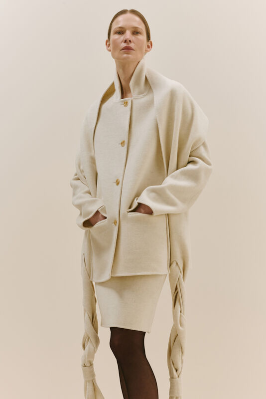 Объемный бежевый жакет с крупными карманами и асимметричным подолом, дополненный облегающей юбкой и чулками