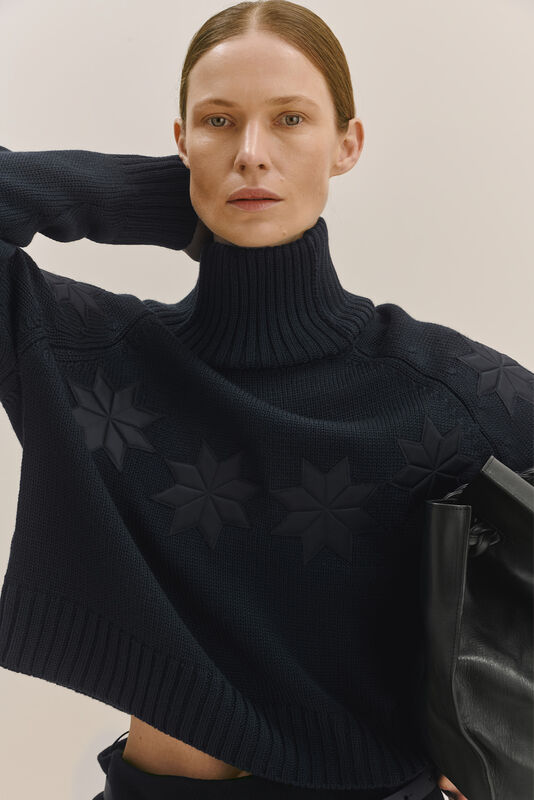 Темно-синий свитер с высоким воротником и рельефными звездами, строгий стиль с акцентом на детали