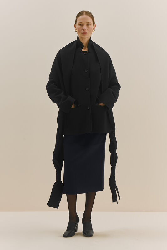 Объемный черный жакет с длинными рукавами и карманами, дополненный строгой юбкой и элегантными туфлями