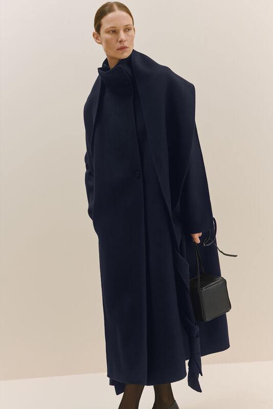 Длинный черный плащ с высоким воротником, элегантный силуэт и минималистичная сумка в руке