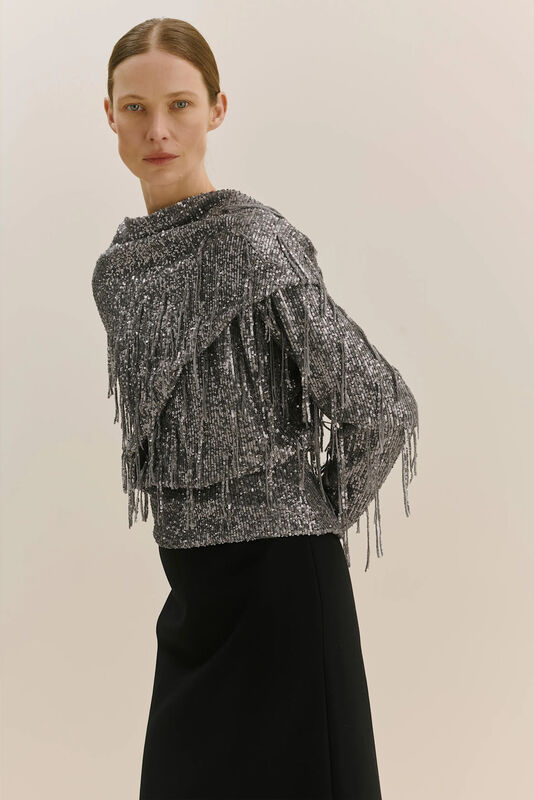 Серебристый топ с бахромой и блестками, гармонично сочетающийся с черной юбкой, создает стильный и вечерний образ