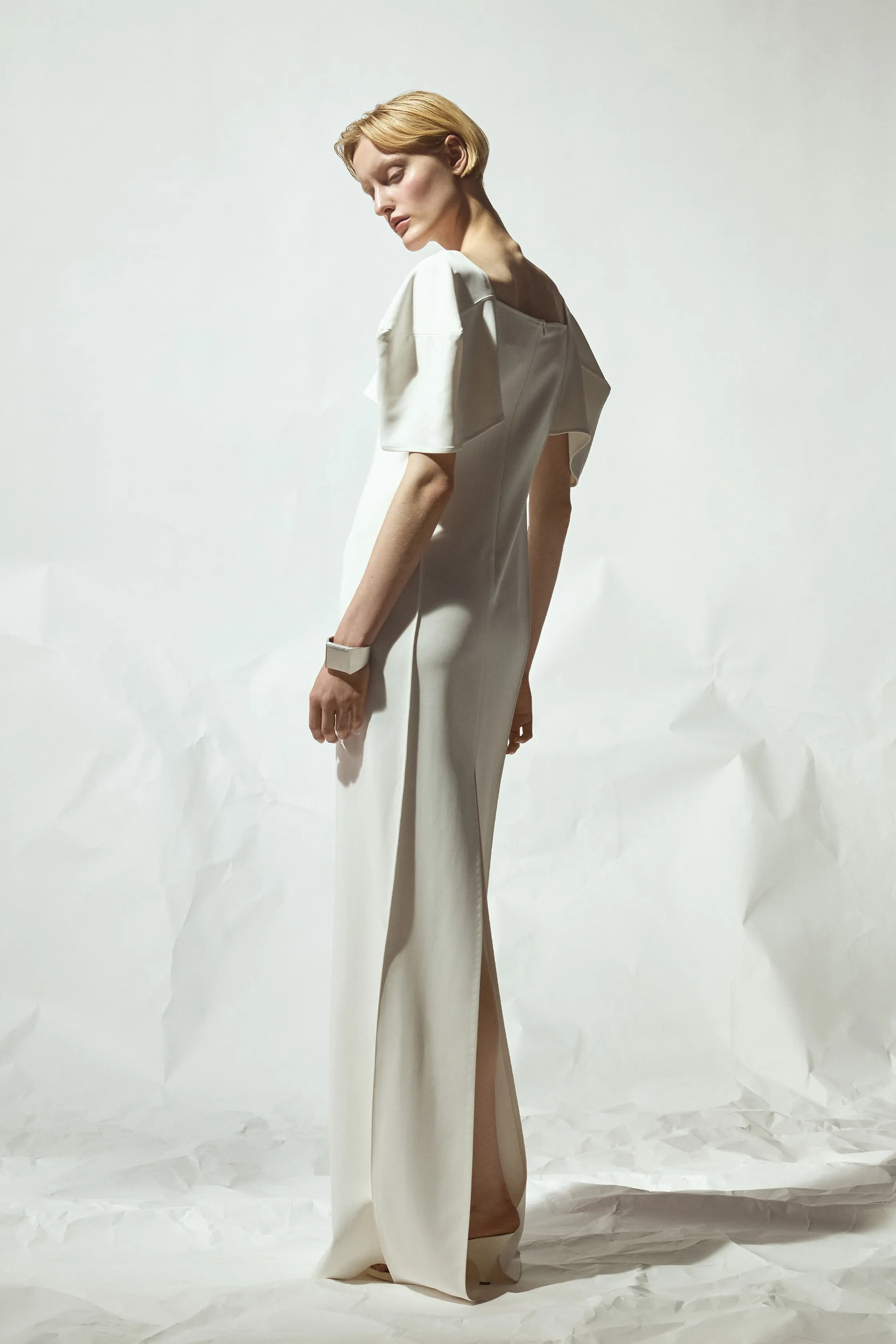 Элегантное белое платье с объемными рукавами, подчеркивающее силуэт, на фоне текстурированной бумаги