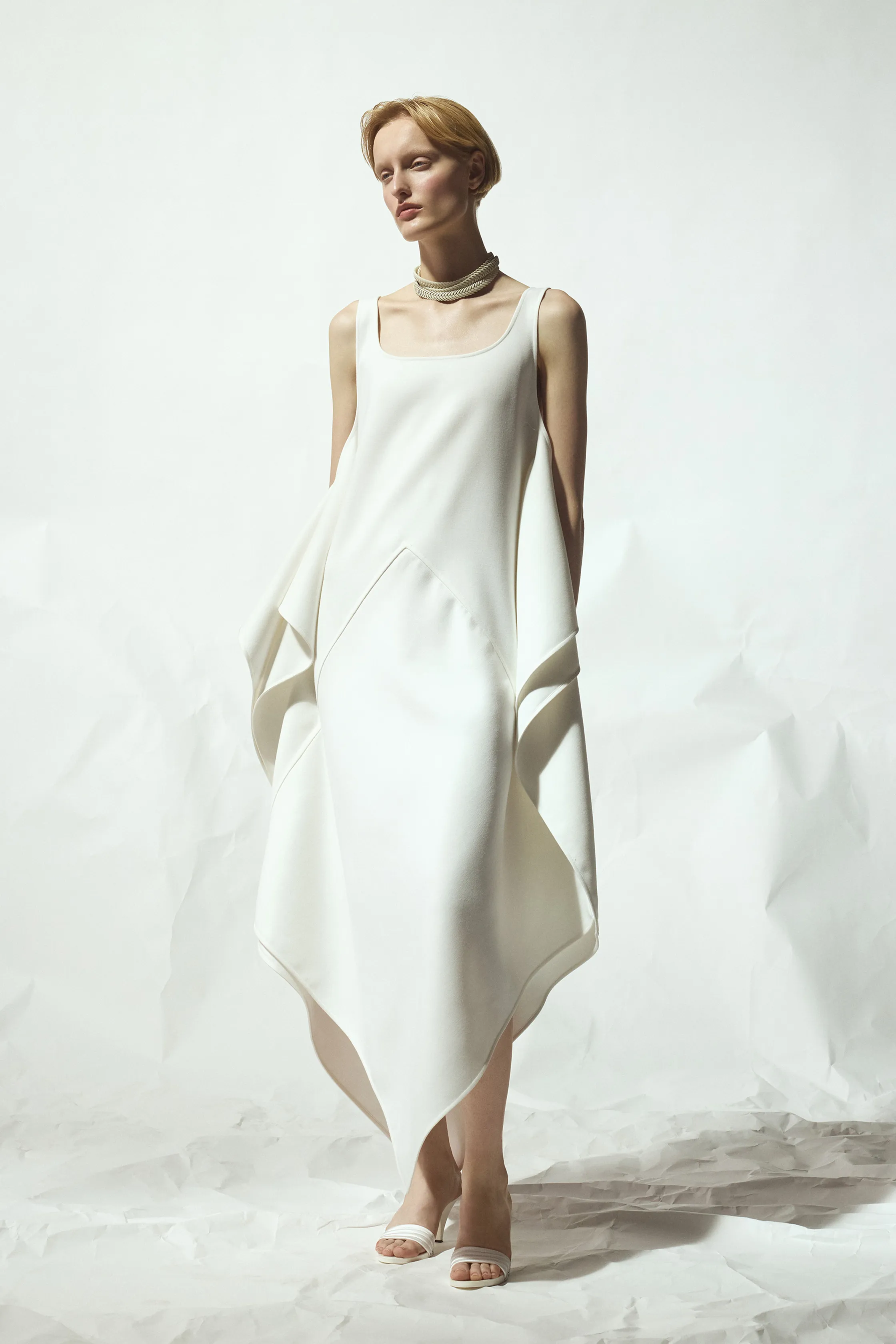 Минималистичное белое платье с асимметричным подолом и драпировкой, дополненное стильным ожерельем