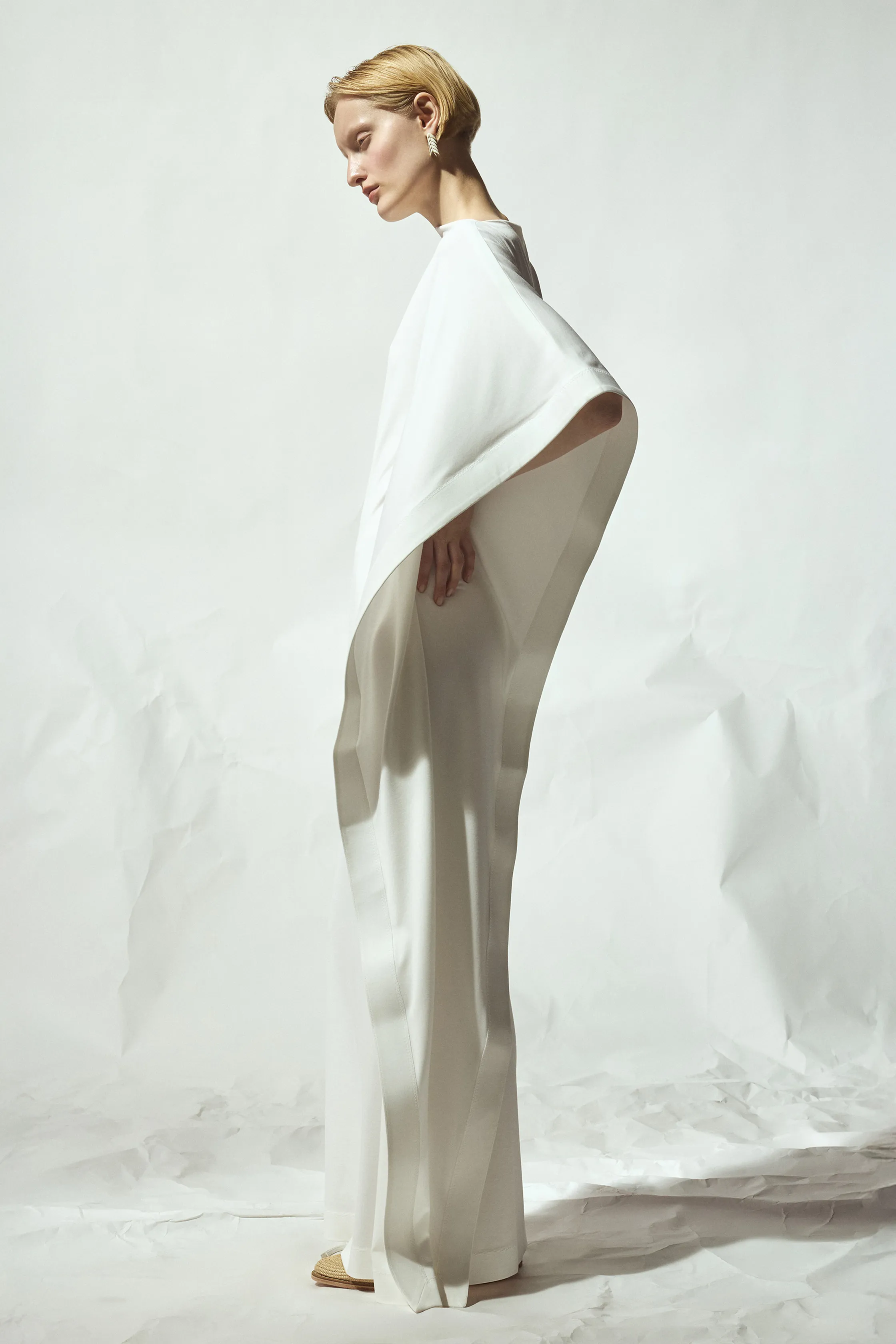 Просторное белое платье с широкими рукавами, изящно обрамляющее фигуру, на фоне нейтрального фона