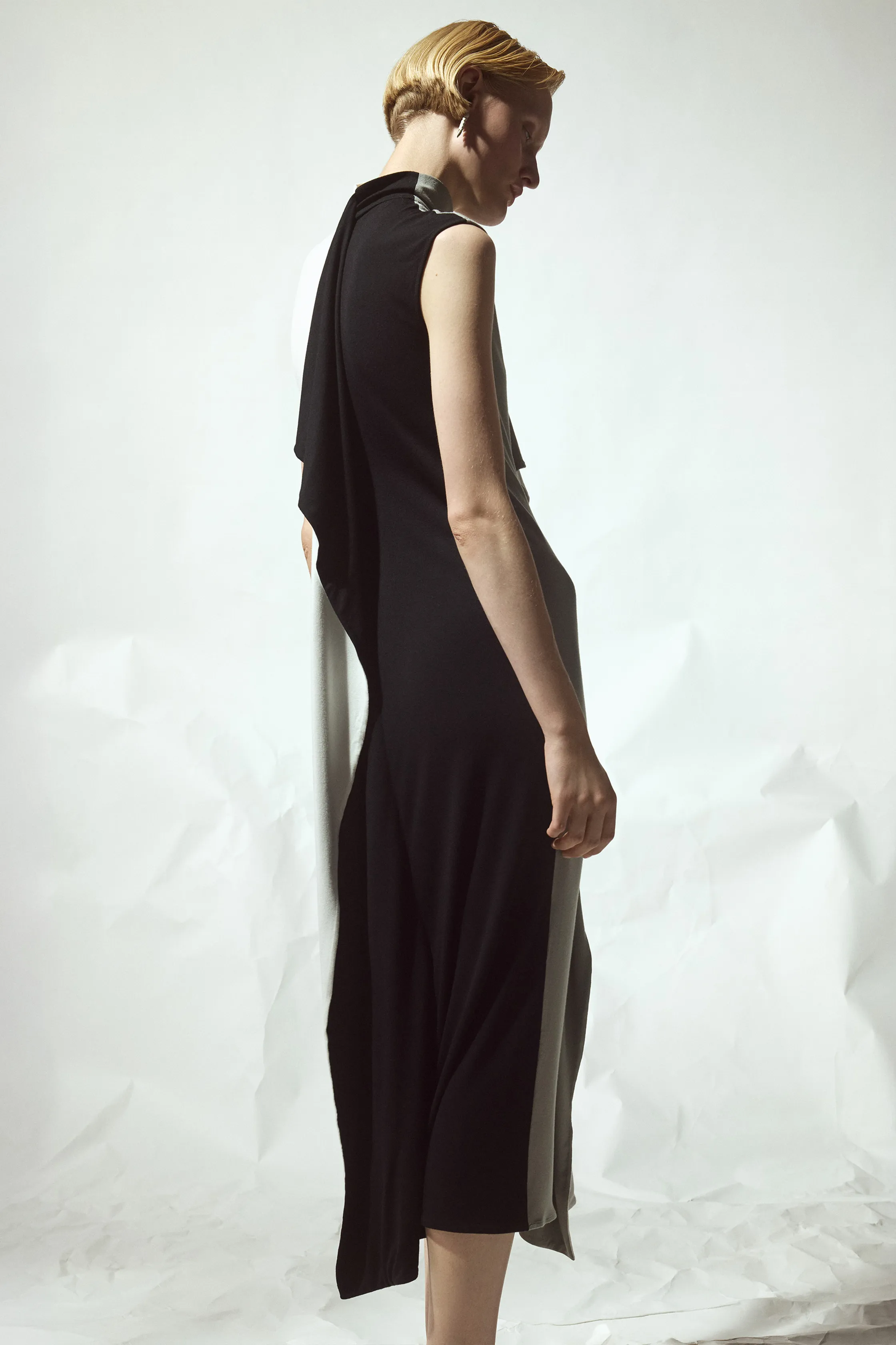 Обтягивающее черное платье с асимметричными деталями, плавно переходящими в светлую ткань, создает эффект легкости и грации