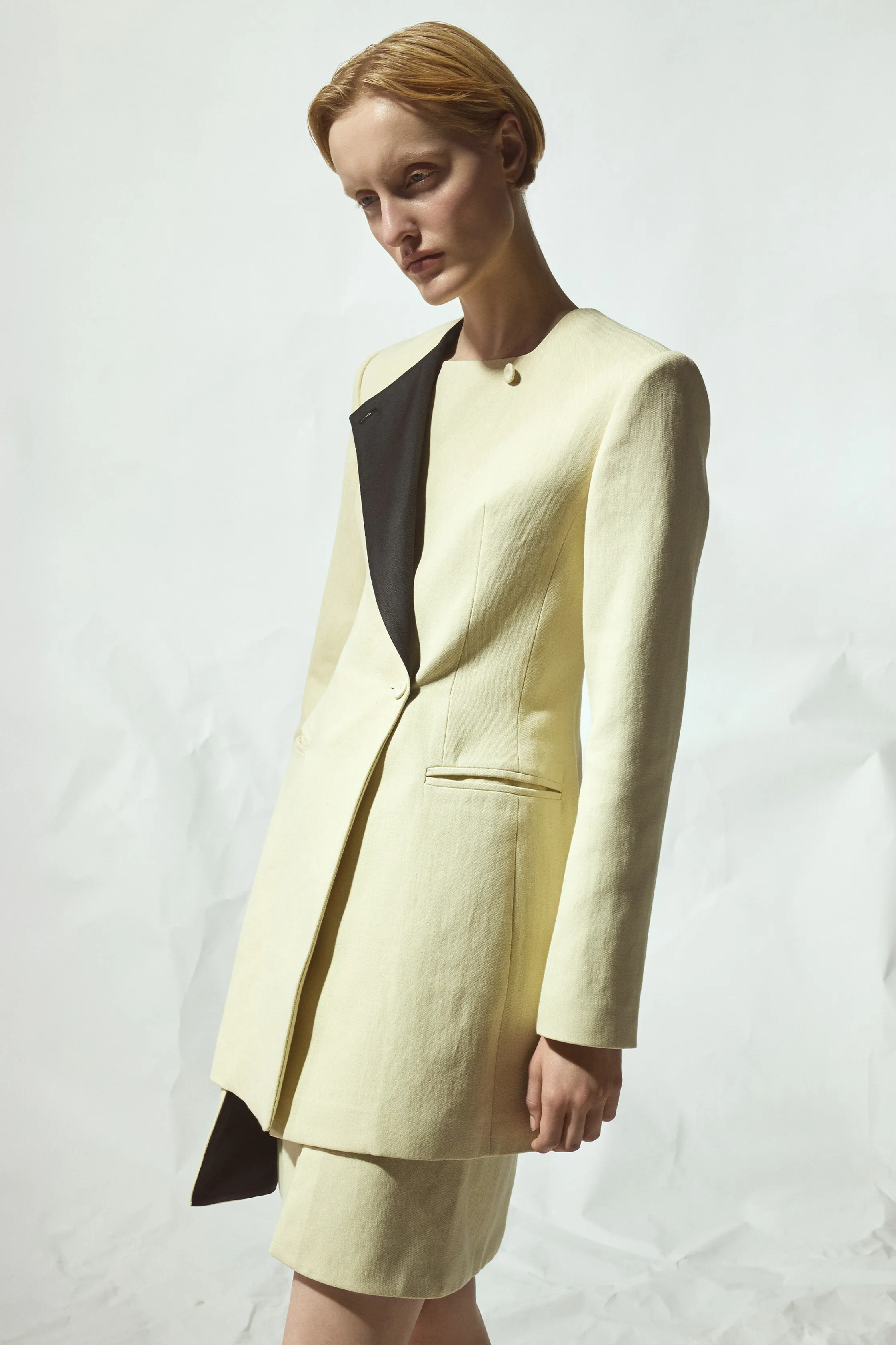 Легкий жакет с асимметричным черным лацканом и короткой юбкой в нежном лимонном оттенке, создающий элегантный силуэт