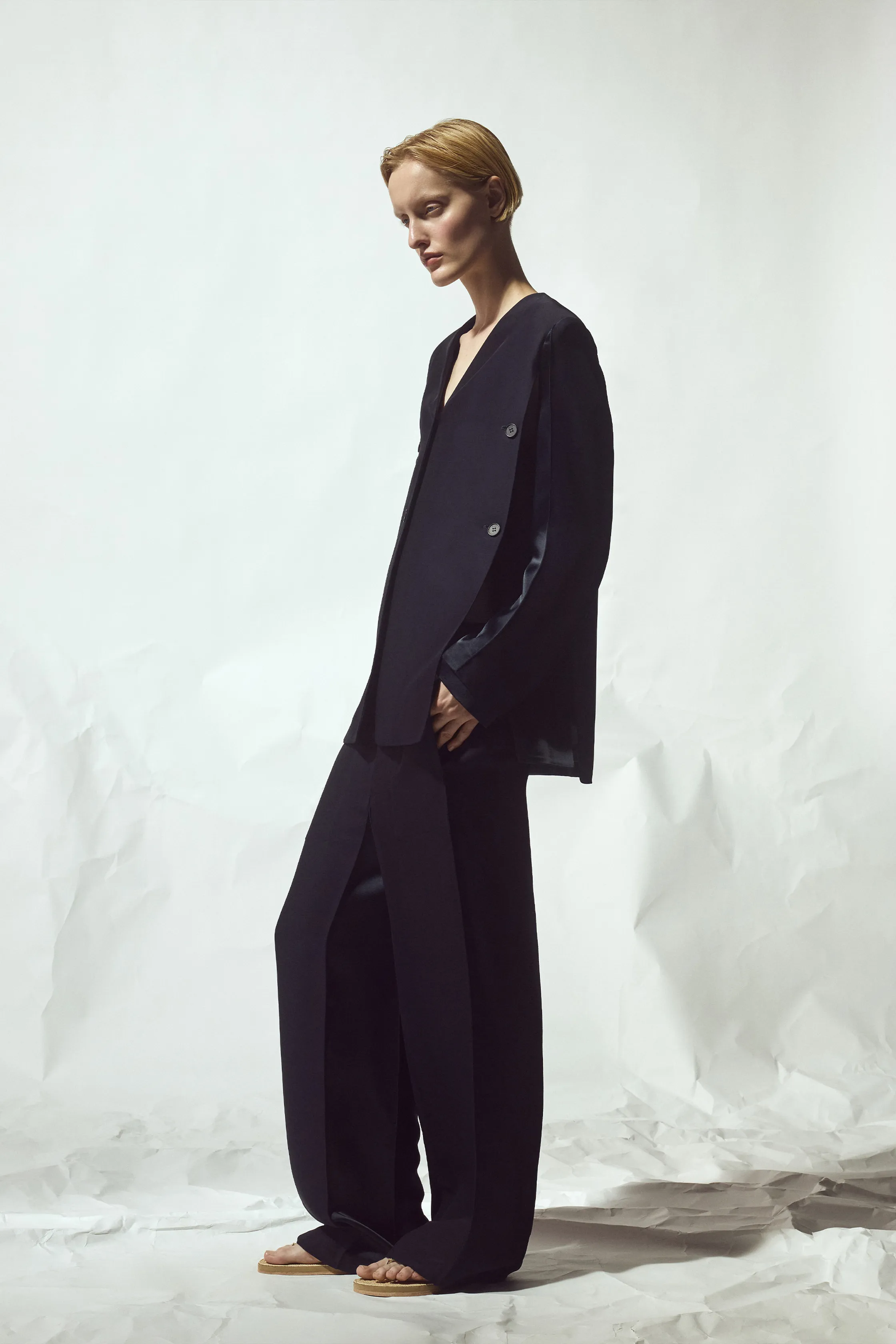 Объемный черный костюм с глубоким вырезом и широкими брюками, создающий эффектный контраст с минималистичным фоном