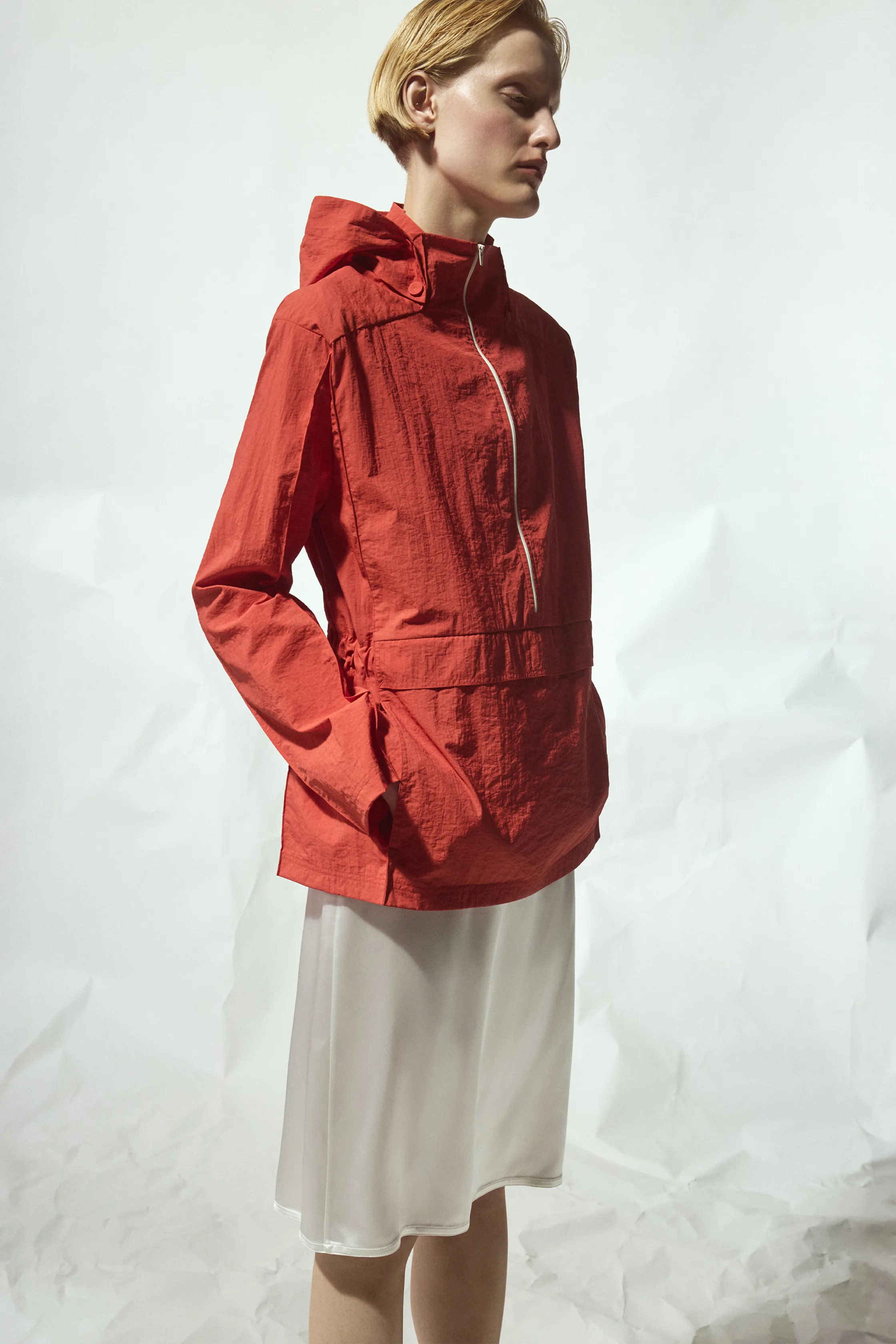 Яркая красная куртка с капюшоном и утонченным кроем, дополненная легким белым платьем, создающим свежий весенний образ