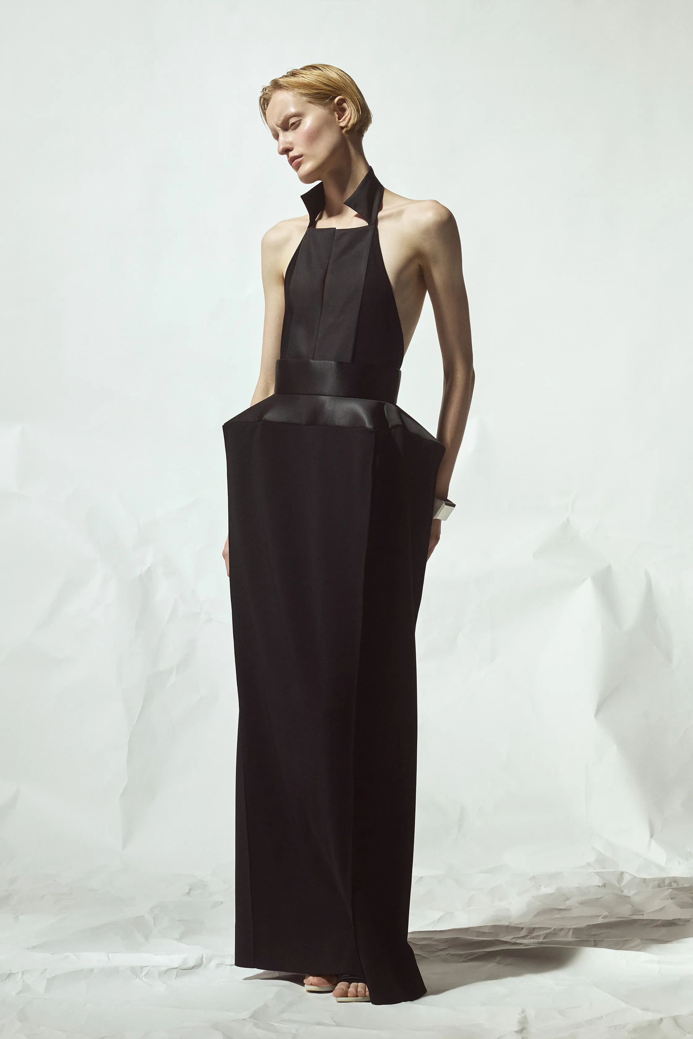 Элегантное черное платье с глубоким вырезом и объемным поясом, создающее контраст с минималистичным фоном