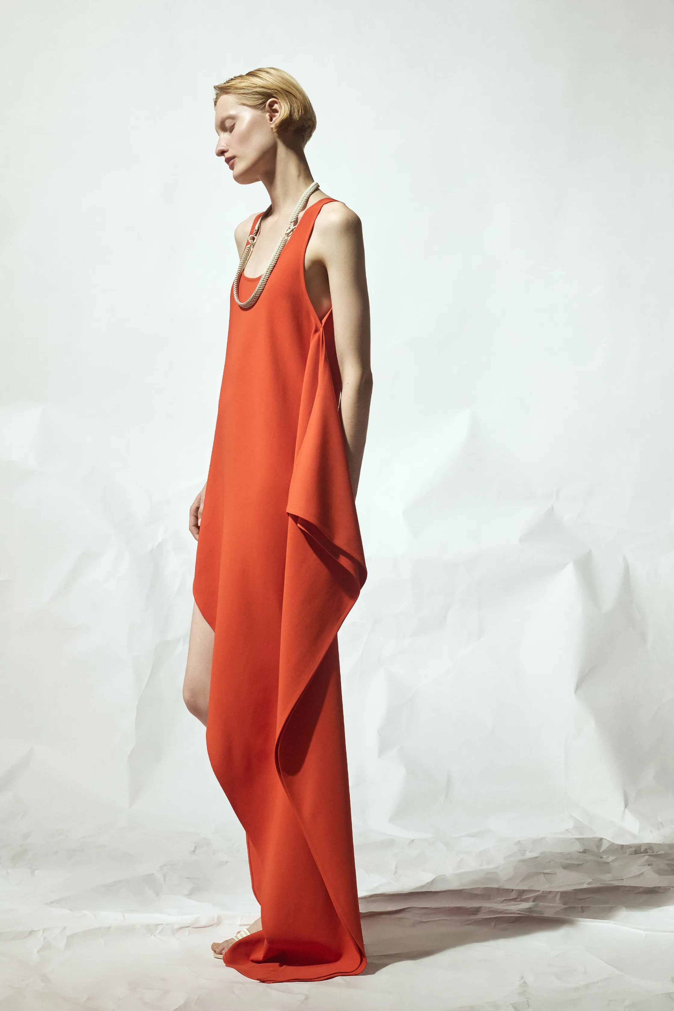 Яркое оранжевое платье с асимметричным кроем и легкой текстурой, дополненное изысканным ожерельем