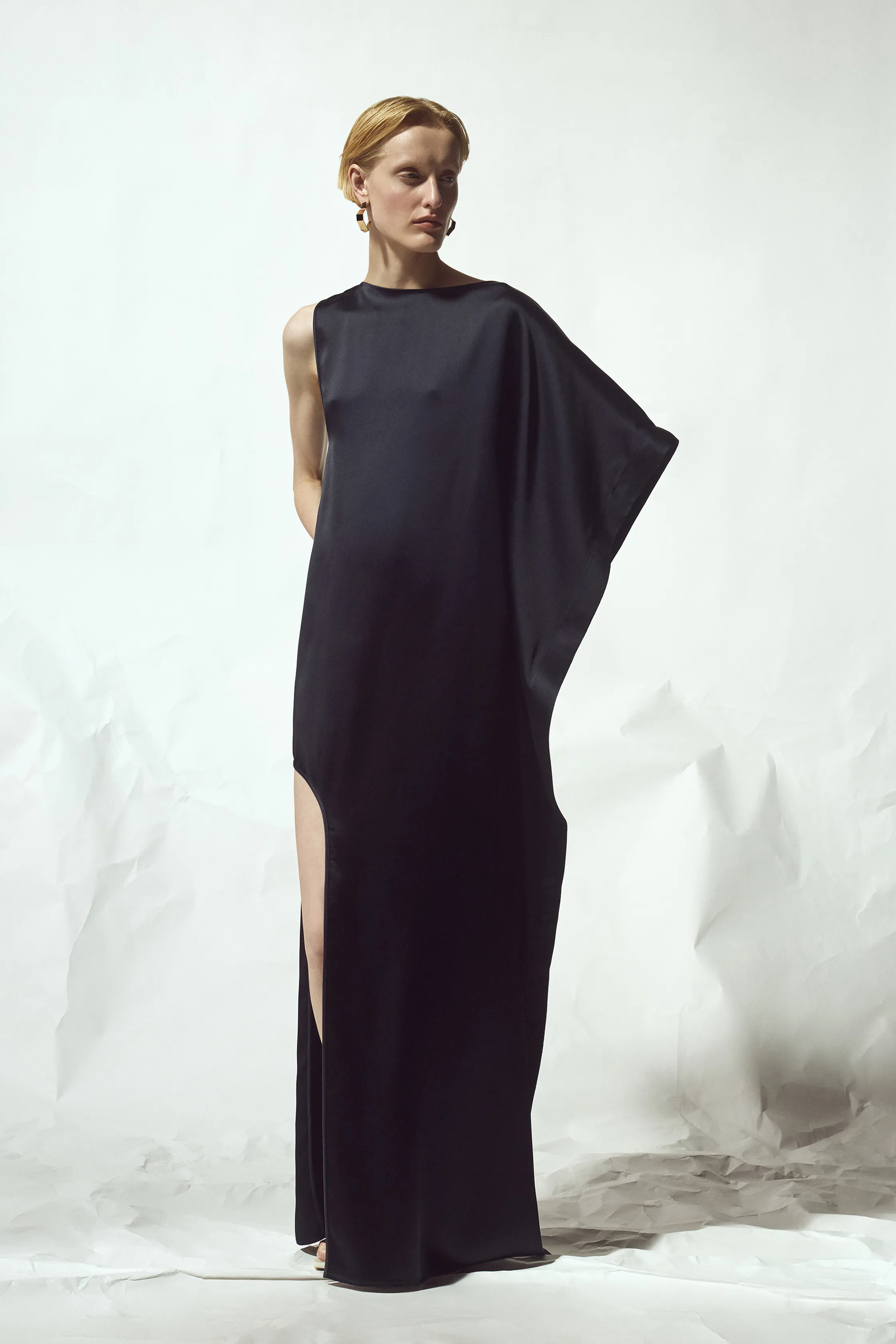 Элегантное черное платье с одним рукавом и высоким разрезом, создающее эффект струящейся ткани