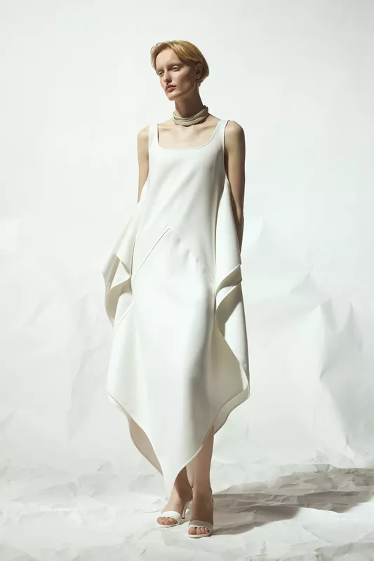 Минималистичное белое платье с асимметричным подолом и драпировкой, дополненное стильным ожерельем
