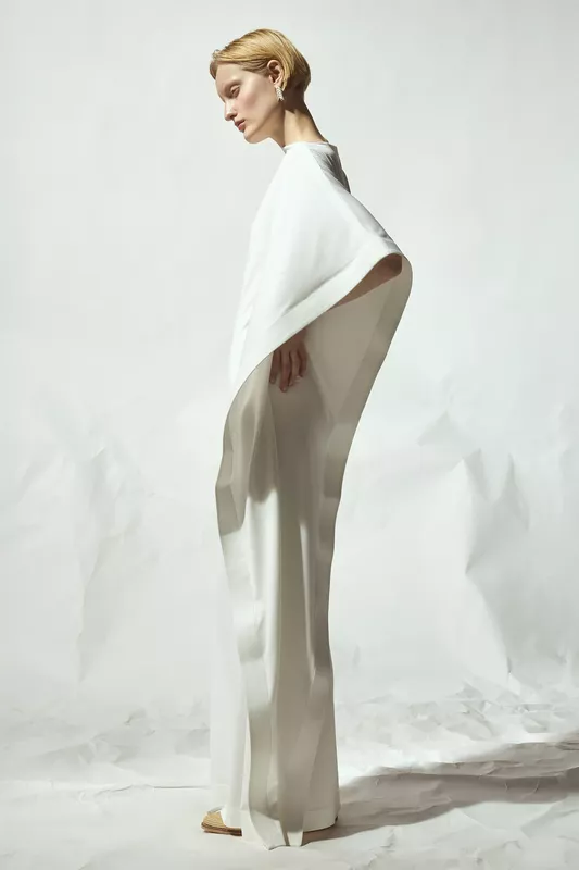 Просторное белое платье с широкими рукавами, изящно обрамляющее фигуру, на фоне нейтрального фона