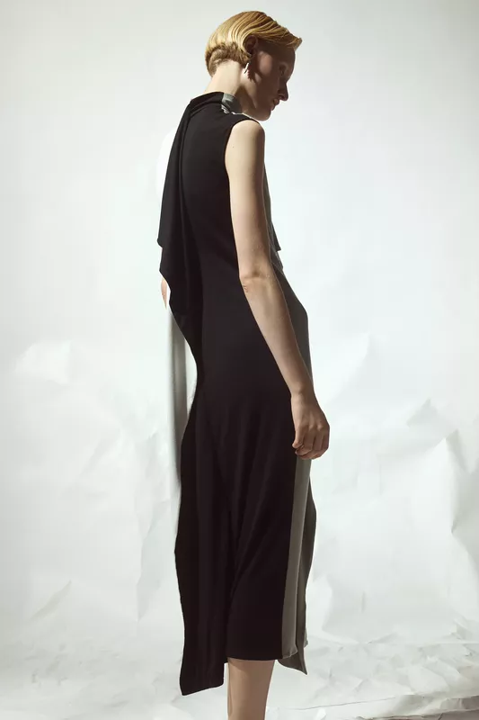 Обтягивающее черное платье с асимметричными деталями, плавно переходящими в светлую ткань, создает эффект легкости и грации