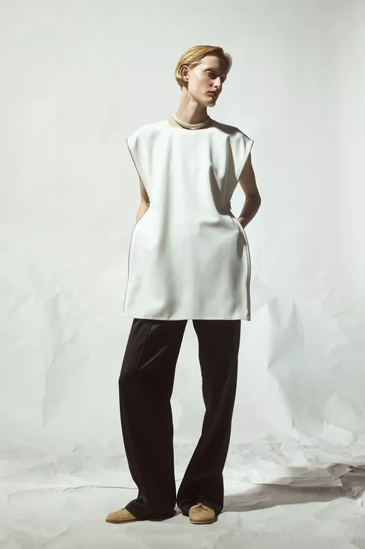 Белая туника с объемными рукавами и карманами, гармонично сочетающаяся с черными брюками, создавая стильный контраст