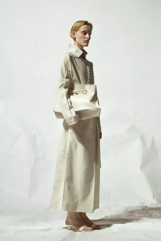 Строгий наряд из светлого материала с высоким воротником и объемной сумкой, подчеркивающий утонченность образа