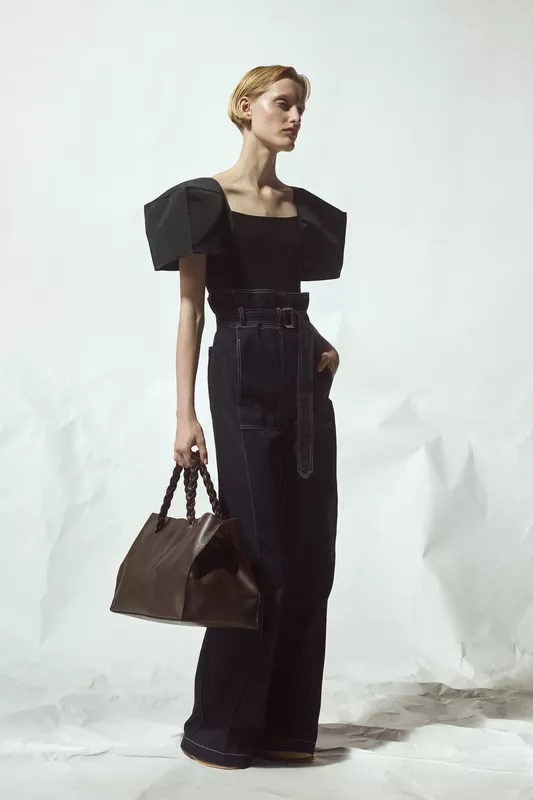 Черный топ с объемными рукавами и высокие джинсы с поясом, гармонично сочетающиеся с коричневой сумкой, создающей стильный акцент