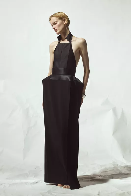 Элегантное черное платье с глубоким вырезом и объемным поясом, создающее контраст с минималистичным фоном