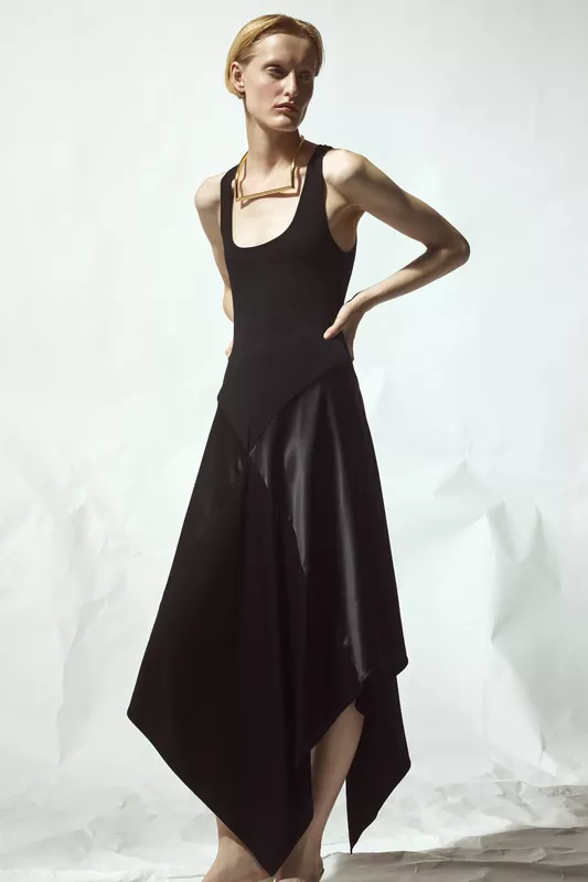 Минималистичное черное платье с асимметричным подолом и глубоким вырезом, дополненное золотым ожерельем