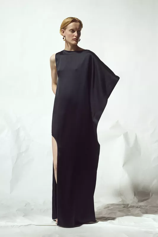 Элегантное черное платье с одним рукавом и высоким разрезом, создающее эффект струящейся ткани
