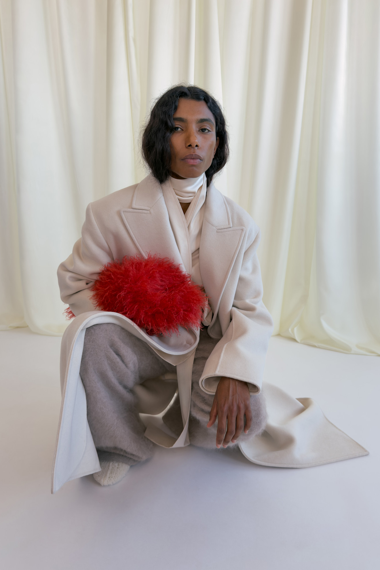 Элегантный светлый плащ с красным аксессуаром из меха, дополненный мягкими серыми брюками и белым шарфом