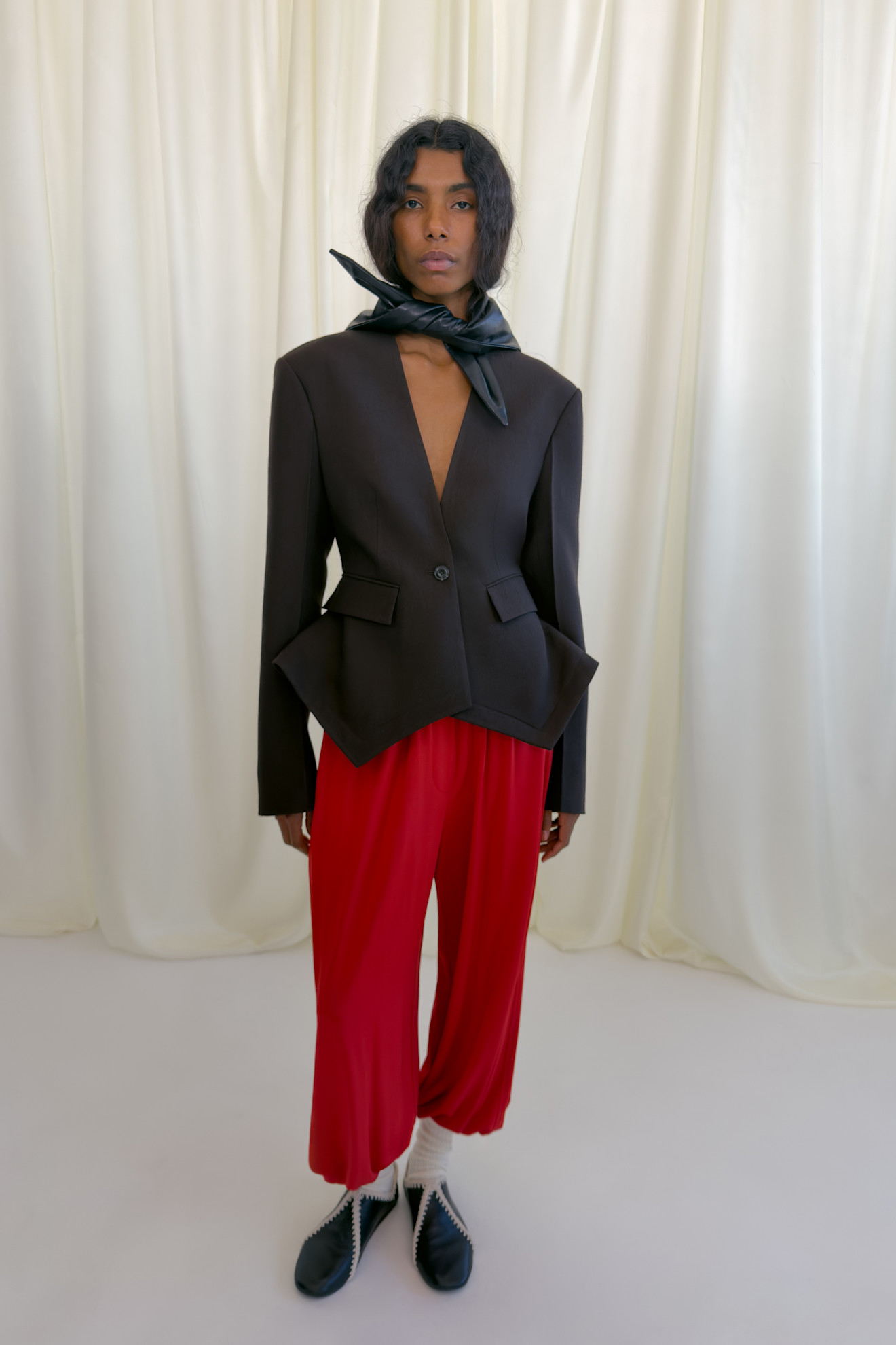 Строгий черный жакет с акцентом на талии и яркие красные брюки, завершенные черным шелковым платком