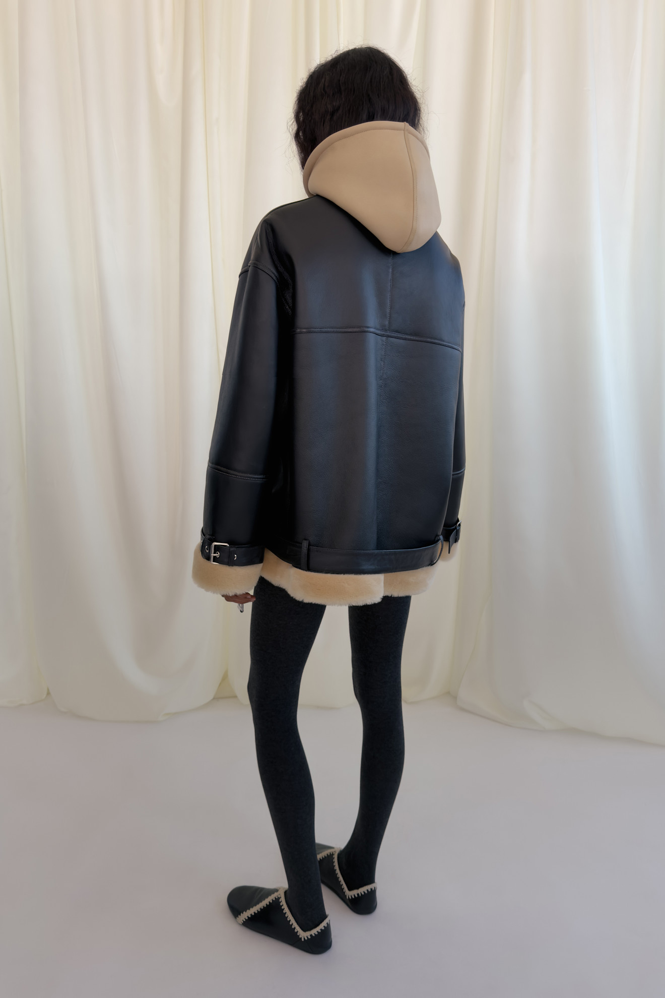 Объемная черная куртка с бежевым капюшоном и меховой отделкой, дополненная леггинсами и уютными тапочками