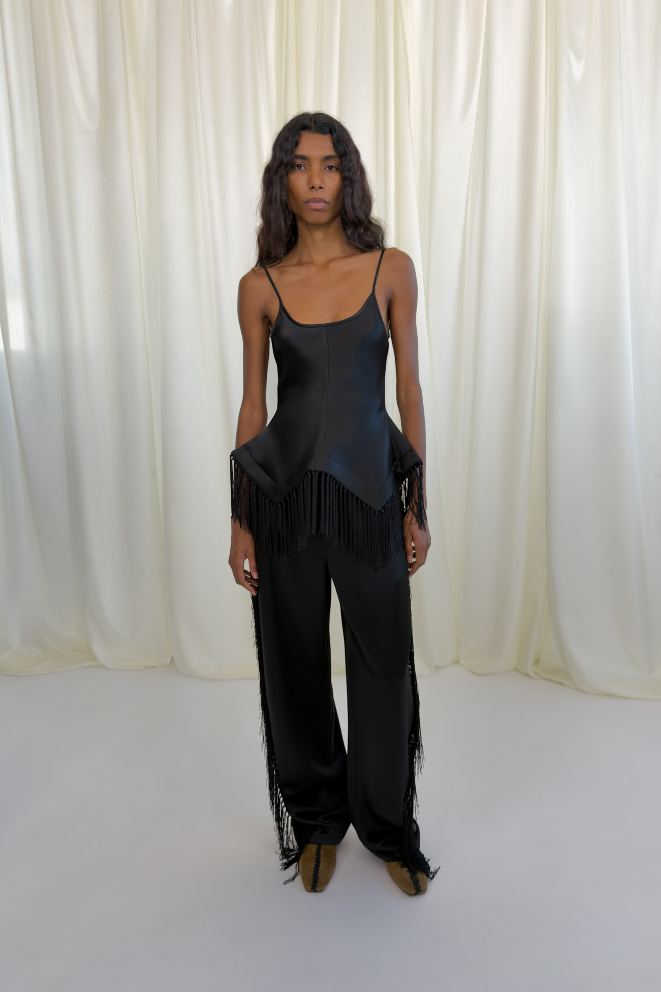 Лаконичный черный топ с бахромой и широкие брюки из гладкой ткани создают элегантный образ для осени-зимы 2026 от Nanushka