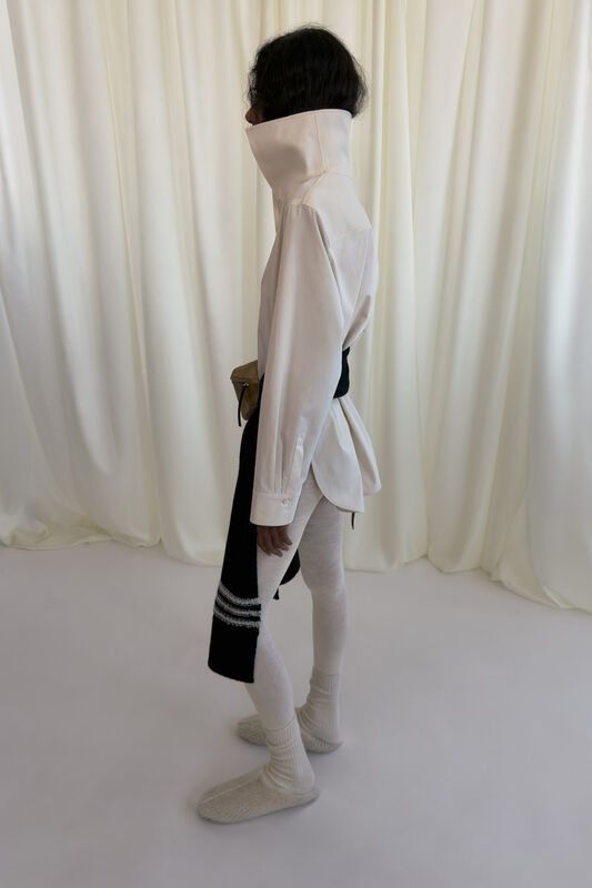 Минималистичная белая рубашка с высоким воротником, обрамленная черным поясом и леггинсами, создающими утонченный силуэт