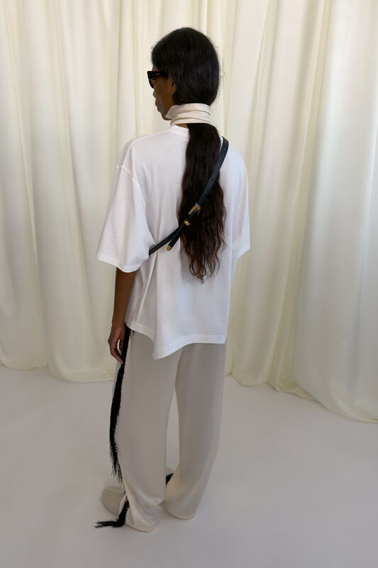 Объемная белая футболка и светлые брюки с черной бахромой создают расслабленный образ в минималистичном стиле