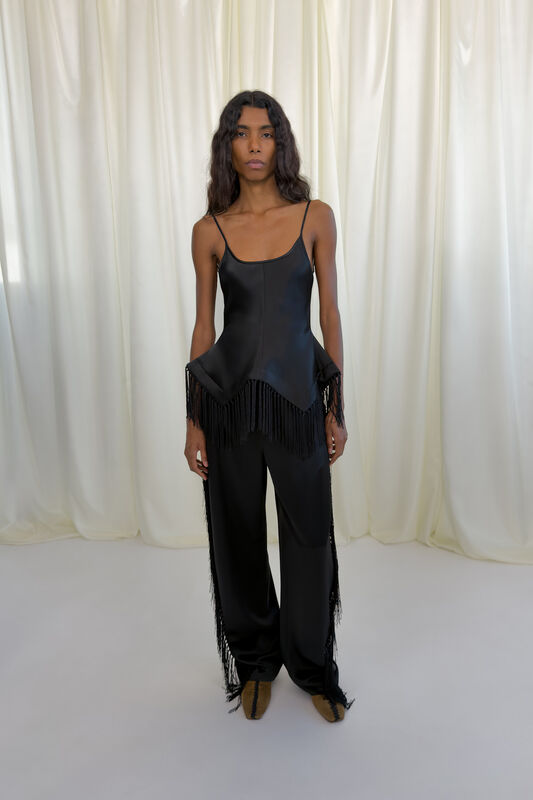 Лаконичный черный топ с бахромой и широкие брюки из гладкой ткани создают элегантный образ для осени-зимы 2026 от Nanushka
