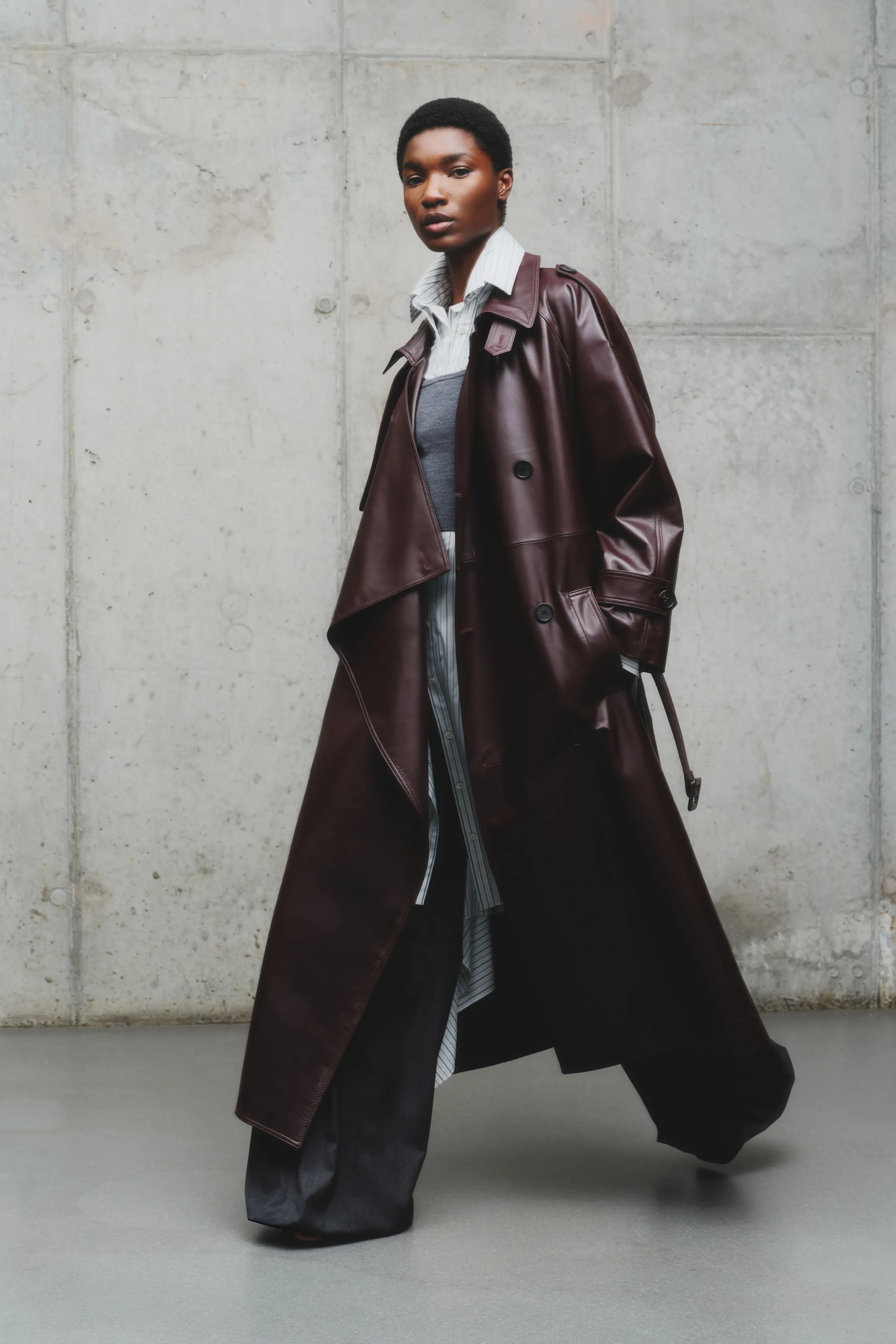 Стильный кожаный плащ глубокого бордового цвета, надетый поверх многослойного наряда с полосатой рубашкой и брюками