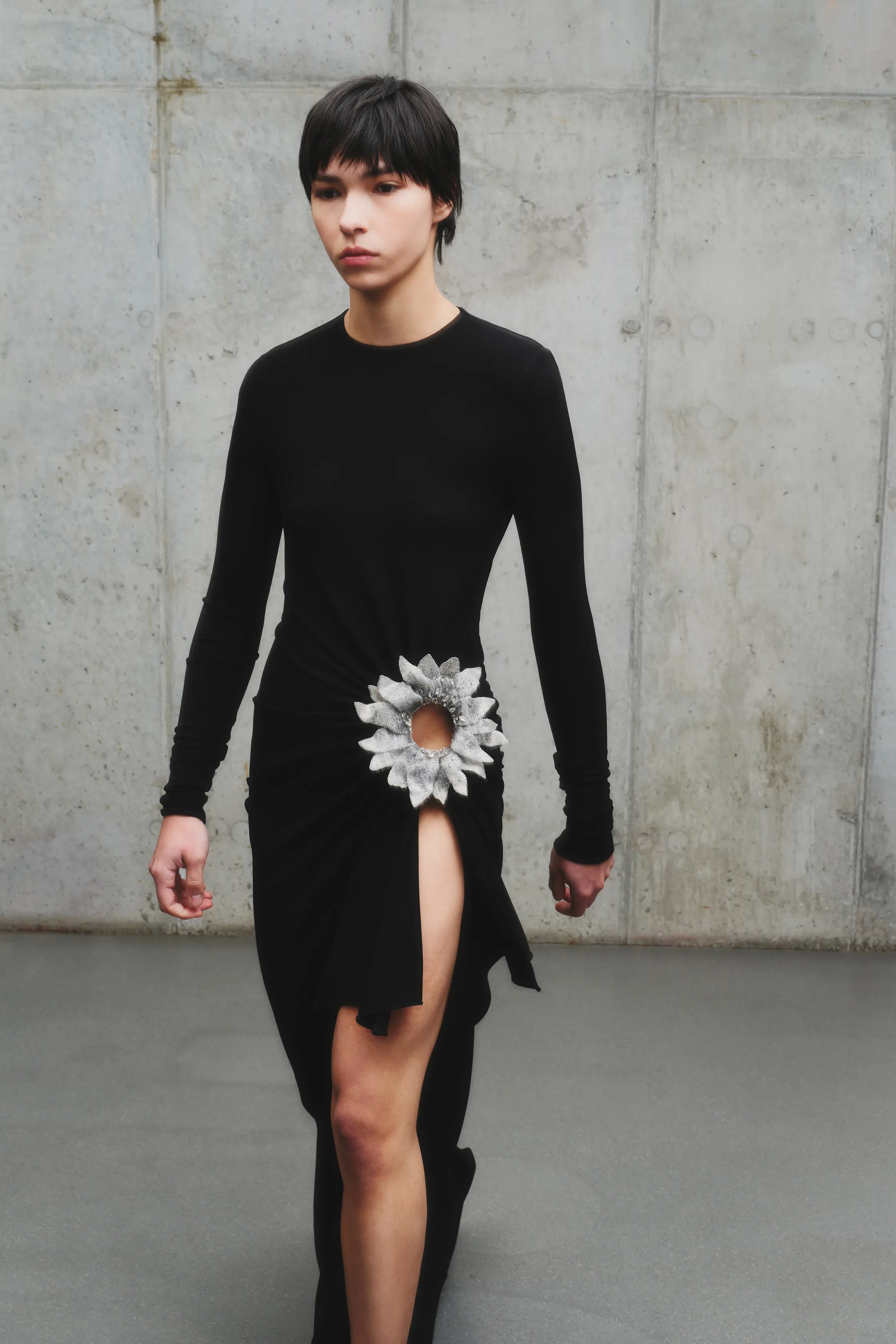 Обтягивающее черное платье с разрезом и декоративным цветком, акцентирующим внимание на талии и создающим эффектный образ