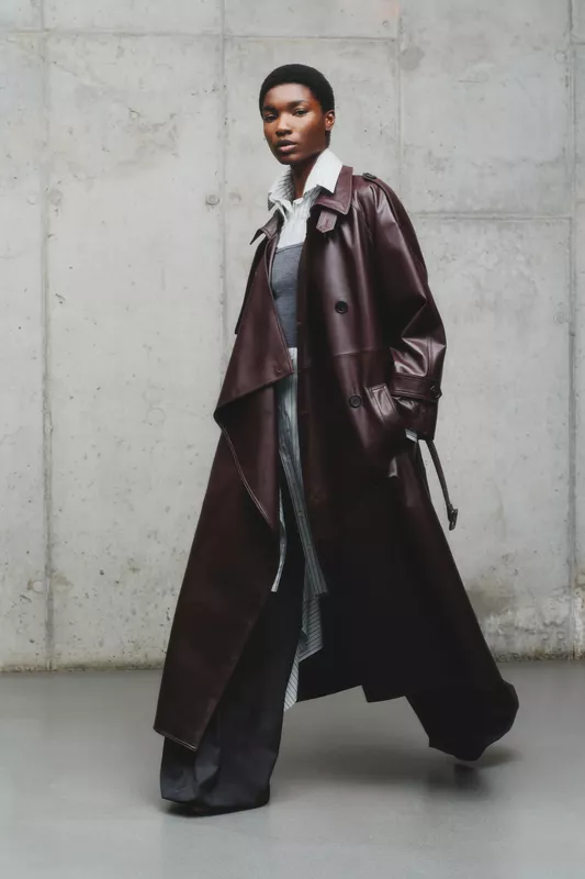 Стильный кожаный плащ глубокого бордового цвета, надетый поверх многослойного наряда с полосатой рубашкой и брюками
