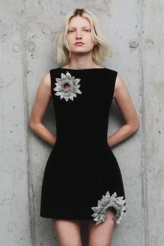 Черное платье с объемными серебристыми цветами, придающими наряду уникальность и изысканность, на фоне бетонной стены